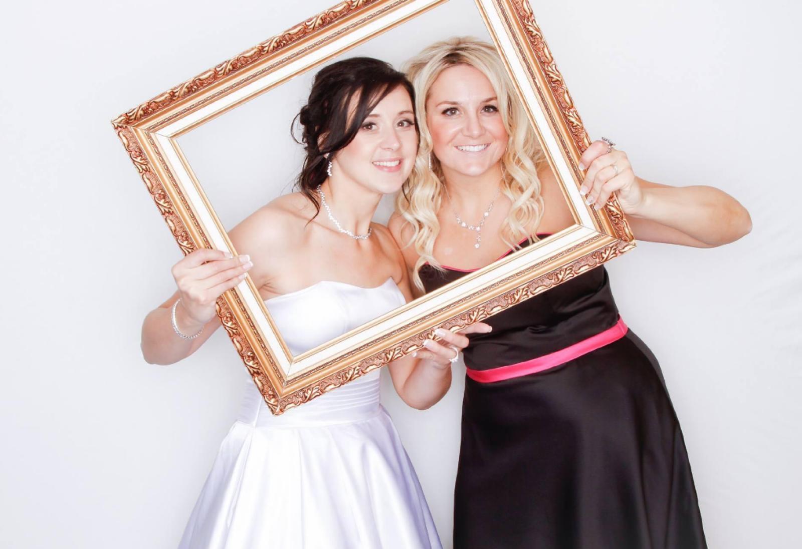 Bride and guest posing with a gold frame prop